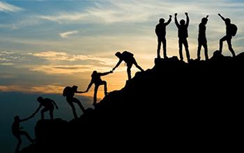 Silhouette of team summitting a mountain during sunset