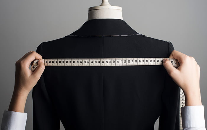 Hands holding a measuring tape across the shoulders of a mannequin