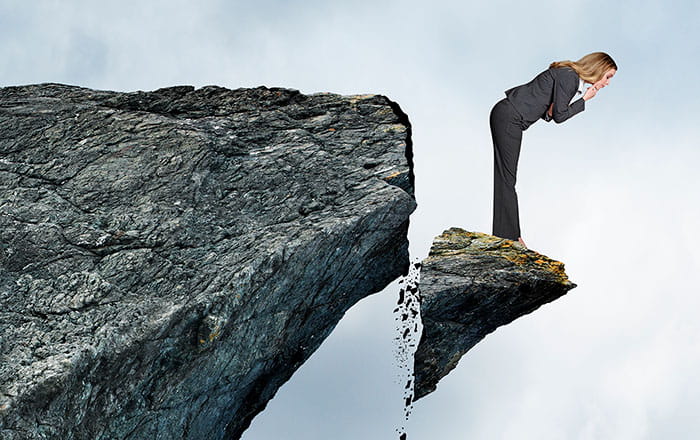 Woman standing on broken off edge of a cliff looking down as it falls